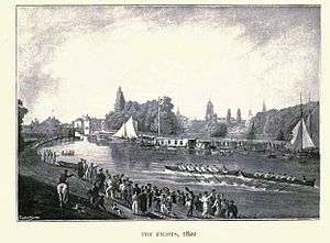 A river scene, with two eight-oared boats racing in the middle of the river, one just in front of the other. There are crowds on each bank and some sailing boats and barges by the far bank. In the distance, trees and church spires.