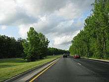 A four-lane limited access parkway lined with trees on the sides and in the median.