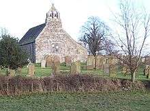 The plain west end of a stone church with a two-light window and a double bellcote surmounted by a saltire finial