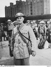 A military officer in a dress uniform with helmet standing on a quayside