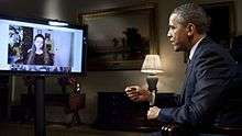 President Barack Obama, seated at right, answers questions about the State of the Union posed by citizens, shown on a flat-screen monitor at left, in the first-ever completely virtual interview from the White House. This interview aired on the official White House Google+ page on January 30, 2012.