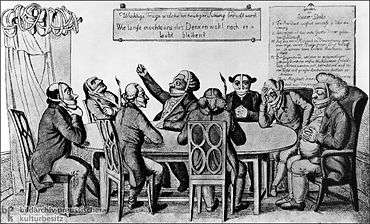 Men sitting around a table. Most of them are muzzled, some are gagged as well, some have blindfolds on, and some have their ears muffled.