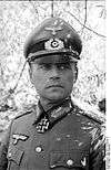 A man wearing a military uniform, peaked cap, and an Iron Cross displayed at the front of his uniform collar.