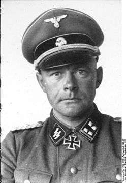 A man wearing a military uniform and peaked cap with an Iron Cross displayed at the front of his uniform collar.