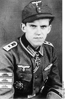 A man wearing a military uniform, side cap, various military decorations including an Iron Cross displayed at the front of his uniform collar.