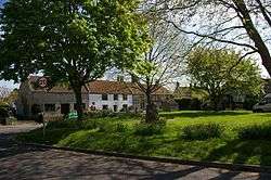 Grassy area with trees in the foreground and a terrace of stone houses, one white fronted, in the background