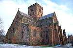 A bulky red-stone building with transepts and a central battlemented tower