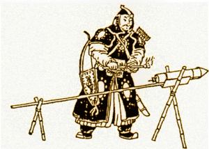A man in black armor standing in front of a rocket, attached to a stick, with the stick being held up by two X-shaped wooden brackets.