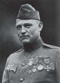 Head and shoulders of a man in a neatly pressed military uniform with four medals hanging from ribbons on his chest and a garrison cap.