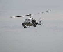 A helicopter flying with four special police troops standing on its landing skids