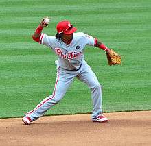 A young, dark-skinned man with dreadlocks throwing a baseball with his right hand