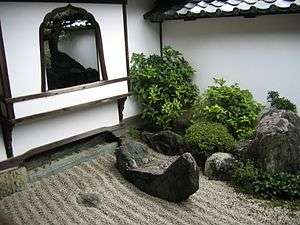 A wall with window and a raked stone garden.