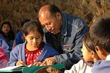 Middle-aged amle teacher helping a young girl as her classmates watch