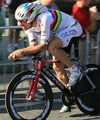 A cyclist wearing a rainbow skinsuit while riding a bike.
