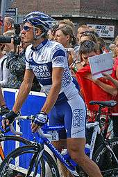 A cyclist standing over a bike while wearing a blue and white uniform.