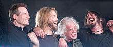 John Paul Jones, Taylor Hawkins, Jimmy Page, and Dave Grohl hugging and smiling onstage
