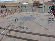 A concrete pad with the state seals of the four states. In the center of the pad is a red disk reading "Four States here meet, in freedom, under God." Inside that disk is a smaller bronze disk.