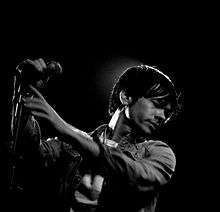 A black-and-white photograph of a man holding up a microphone.