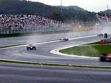 Four Formula One cars are turning left into a corner with spray being lifted from the ground by their tyres.