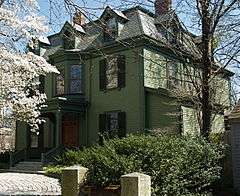 A green three-story house with a mansard roof and small gabled dormers. A small porch protects the entry.