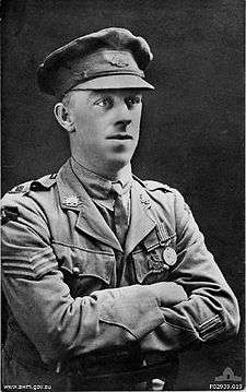 A head and shoulders portrait of a man in military uniform. His arms are crossed.