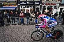 A man riding a bike while wearing a blue, white, and pink skinsuit.