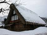 A thatched wooden house with very steep gable covered by snow.