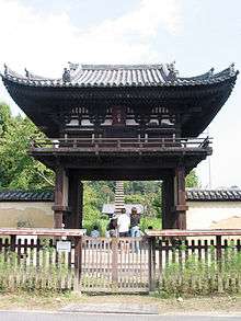 Small, high wooden gate with a railed veranda on the upper floor and a hip-and-gable roof.