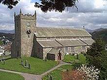 A stone church seen from the northwest with a clerestory and a west tower surmounted by a battlemented parapet and corner pinnacles