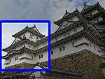 A three-storied castle tower with white walls and a dark roof on a platform of unhewn stones. It is connected to a two-storied structure.