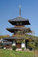 Wooden three-storied pagoda with white walls and railed verandas on the upper floors.