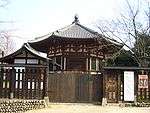 Small octagonal wooden building with white walls and red beams.