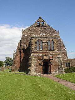 The west end of the stone church with a projecting two-storey porch, large buttresses and a double bellcote