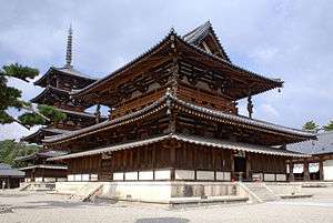 A large wooden building with a hip-and-gable main roof and a secondary roof giving the impression of a two-storied building. Between these roofs there is an open railed veranda surrounding the building. Below the secondary roof there is an attached pent roof. Behind the building there is a five-storied wooden pagoda with surrounding pent roof below the first roof.