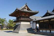 Small wooden tower shaped structure with a flared lower part and a hip-and-gable roof.