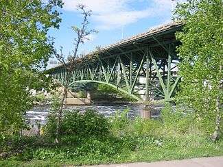 picture of the bridge painted green and surrounded by green foliage seen from the Mississippi bank