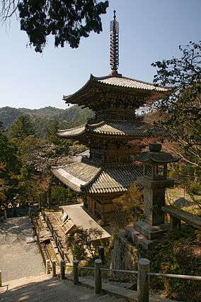 Three-storied wooden pagoda on a hillside.