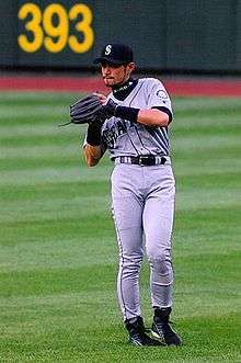 A Japanese man wearing a grey Seattle baseball uniform fielding a ball in the outfield.