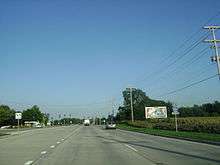 Eastbound IL 22 approaching the traffic signal at Quentin Road. Riding on concrete lanes coming up to the intersection that has dual left turn lanes, two thru lanes, and one right turn lane.