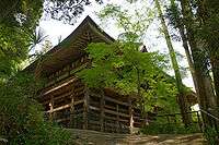 A wooden building with enclosing veranda built on tall wooden pillars.