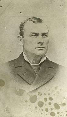 A gentleman posing for a photo in a suit and tie, seen from the chest up.