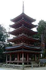 A five-storied pagoda with vermillion red beams and greenish roof. Just below the first-story roof there is an additional pent roof.
