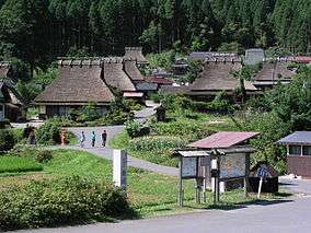 Wooden houses with thatched roofs in a mountain setting.