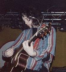 A man performing on-stage with an acoustic guitar.