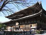 Large wooden building with a hip-and-gable roof and enclosing pent roof.