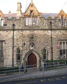 Part of a building with an arched entrance over which is a statue in a niche