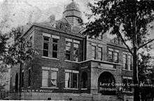 A black and white photograph of a large brick building with two stories and a small dome