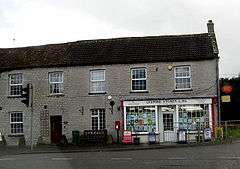 Small shop with white surrounds to the windows set in the right hand building of a terrace.