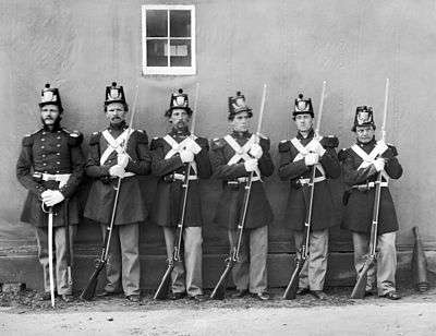 black & white photograph of six Marines standing in line, five with Civil War-era rifles and one with an NCO sword.