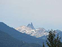 Rugged landscape with a lightly glaciated mountain in the background and forested mountains in the foreground.